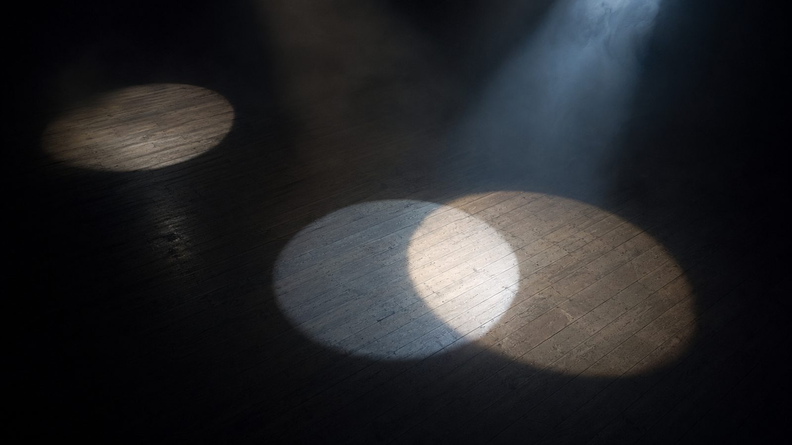 Three spotlight pools on a dark stage floor, two of them overlapping.